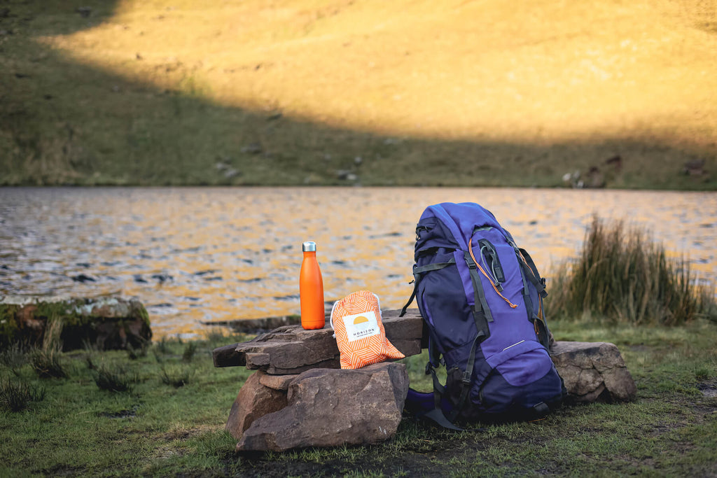 Backpack, water bottle and Horizon Travel Towel lying next to beautiful lake 